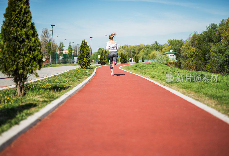 一个女人在跑道上慢跑的后视图。