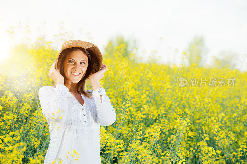 迷人的女人戴着草帽在黄色的田野在夏天