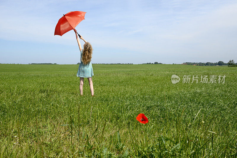 打着红阳伞的少女站在绿色草地上