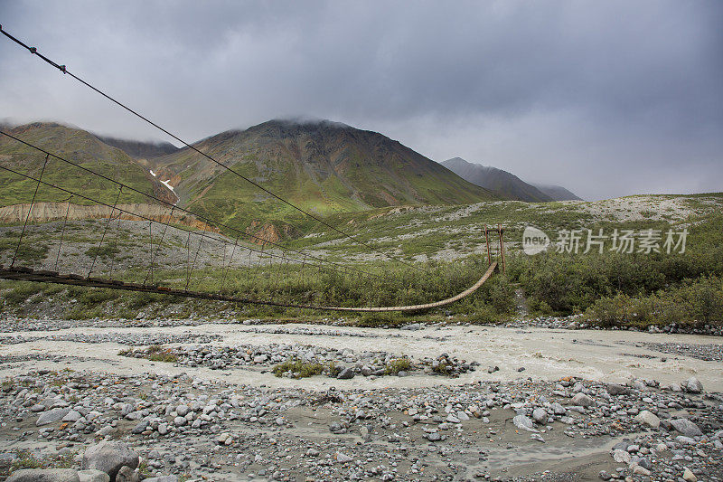 木制悬索桥横跨一条流淌的河流在阿尔