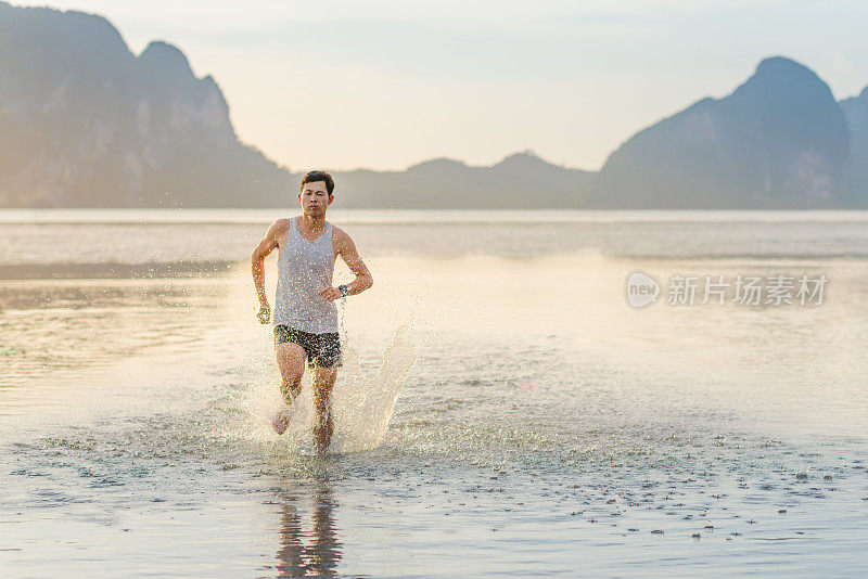 年轻的亚洲男子在海滩上奔跑，夕阳为背景