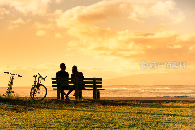 一对夫妇坐在公园长椅上看日落。