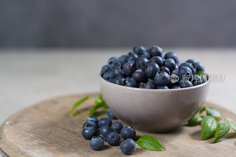 新鲜采摘的多汁蓝莓和绿色的叶子放在质朴的桌子上。木背景上的越桔。蓝莓抗氧化。健康饮食和营养的概念