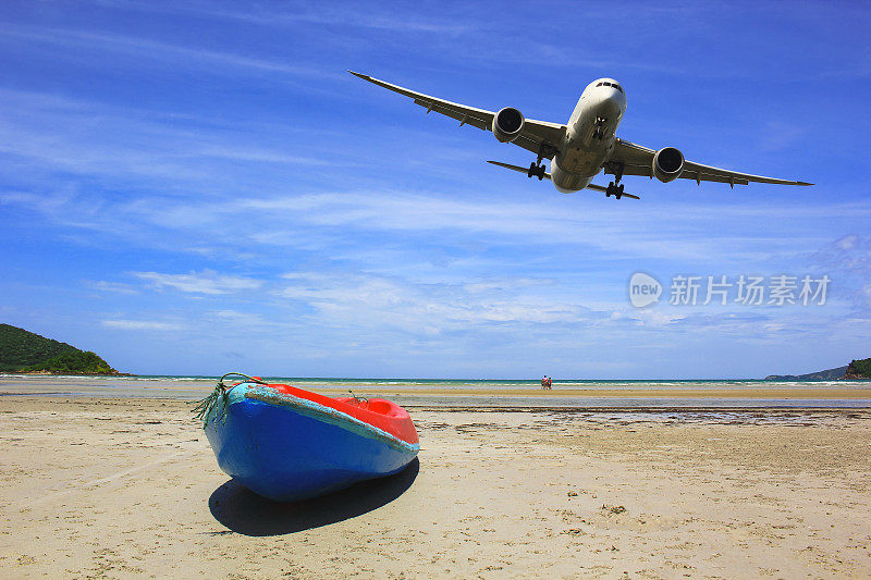 蓝色和红色的皮艇与商业飞机飞过海滩与美丽的蓝天背景
