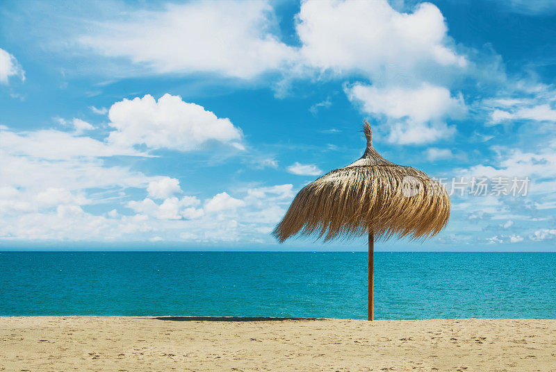 用棕榈叶制成的沙滩伞，站在完美的梦幻天堂，白色的黄色沙滩湾，蓝色的大海和美丽的戏剧性多云的天空。一个放松和度假的地方，在水。