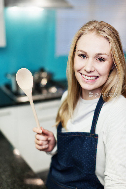 美丽的金发女人在厨房拿着木勺，微笑着