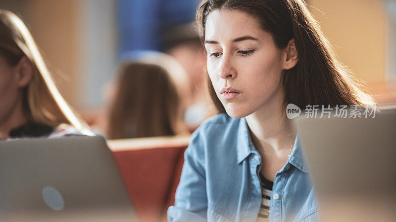 漂亮的年轻女孩学生在现代教室听讲座的同时使用笔记本电脑。聪明的年轻人在大学学习。