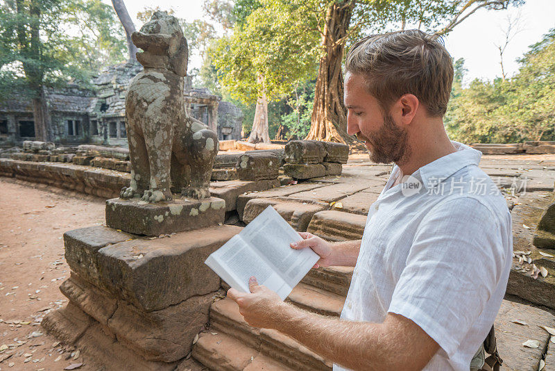 一个年轻人正在柬埔寨的古庙里阅读旅游指南