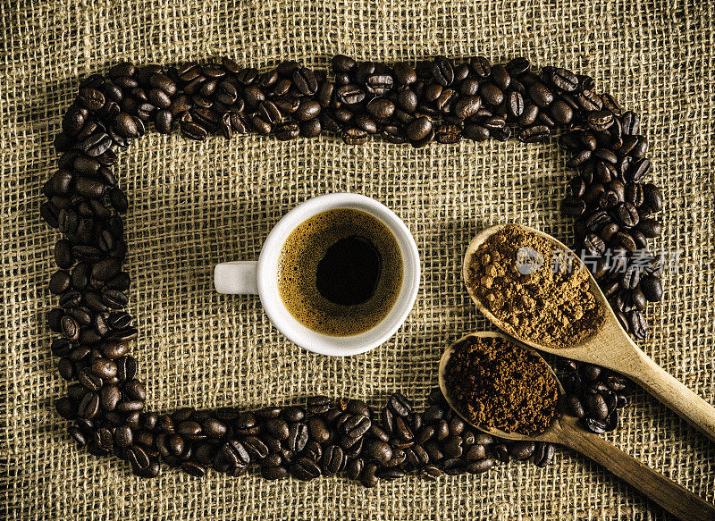 一杯浓缩咖啡和烤生咖啡豆在黄麻背景上做一个框架