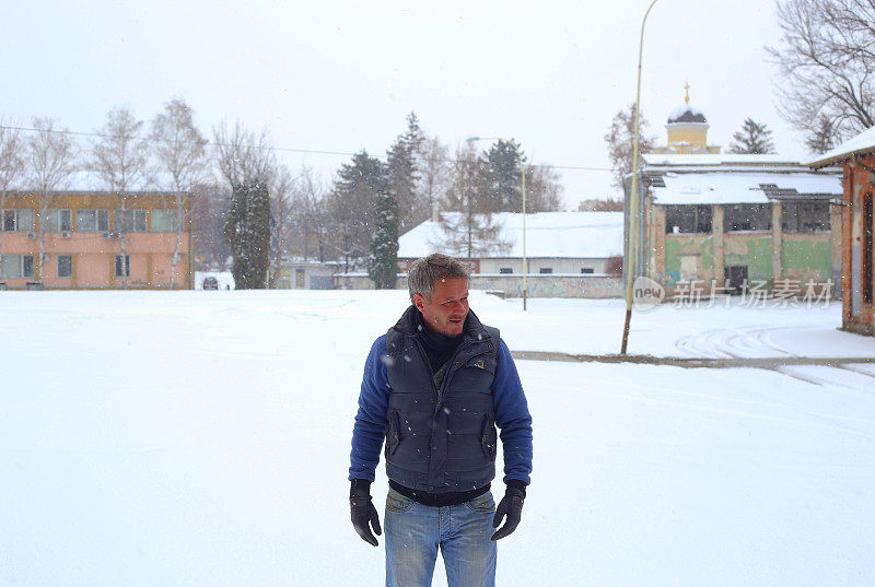 一个白发苍苍的成年男子在大雪纷飞的冬天走在城市里