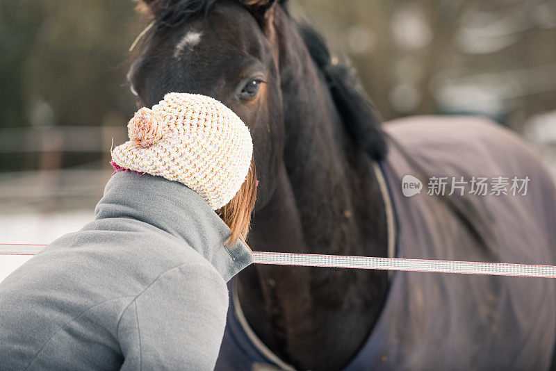 深褐色的女人在冬天拜访马，试图与一匹黑马接触