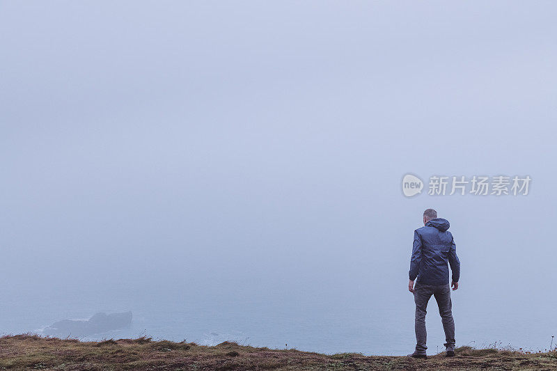 一个人孤零零地站在悬崖边上，俯瞰着浓雾中的大海。