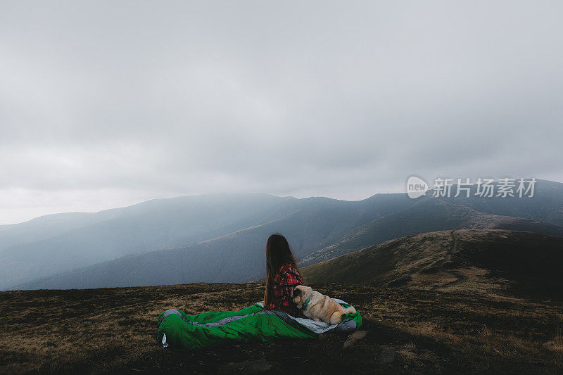 睡袋里的女人和狗在山中醒来