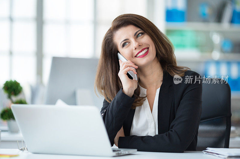 年轻的商业女性在办公室里，用智能手机聊天