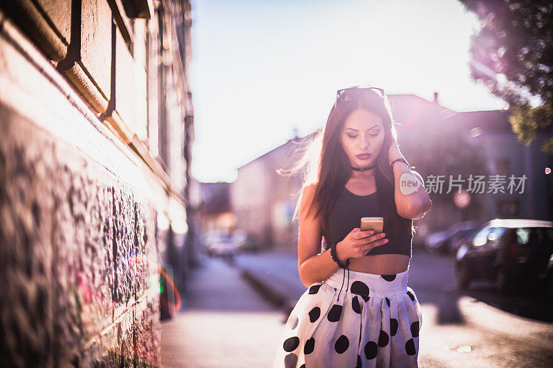 美丽的年轻女子走在城市的街道上，并使用手机