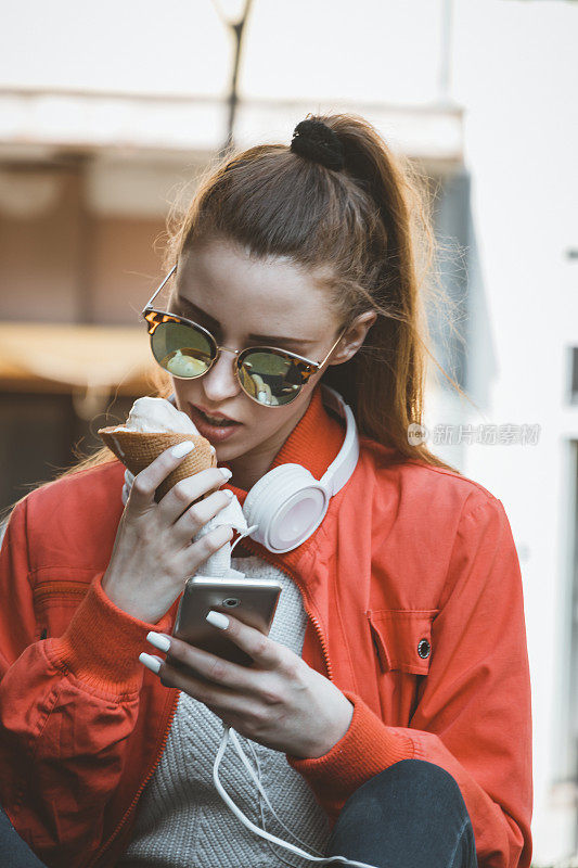 吃着冰淇淋的迷人女人正坐在户外，用智能手机输入信息