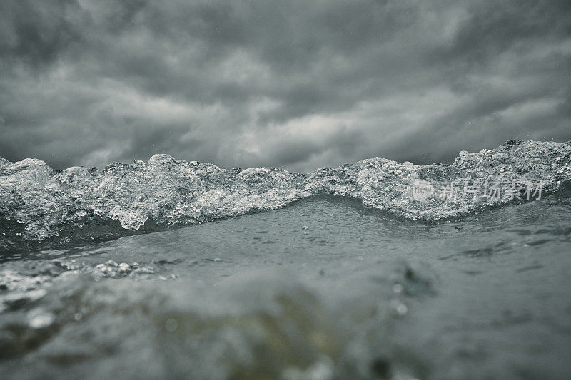 破碎的波浪接近相机在海面上与一个黑暗戏剧性的暴风雨天空。