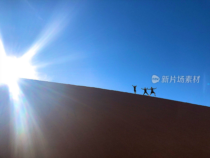 跳跃的男孩在高高的沙丘上的剪影和太阳的耀斑