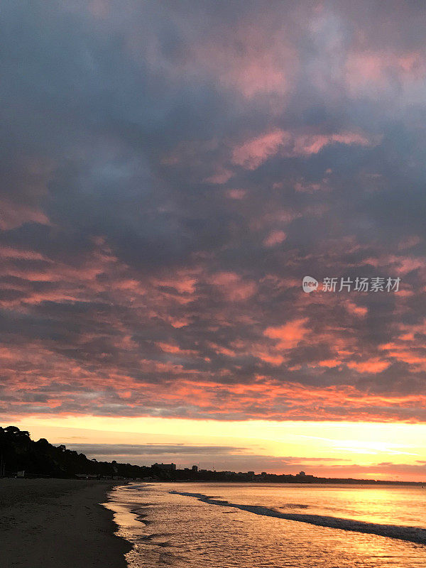 清晨的海滩日出与乌云和粉红色的蓝天，伯恩茅斯海滩日出日落照片，多塞特海岸线，英格兰西南部，英国