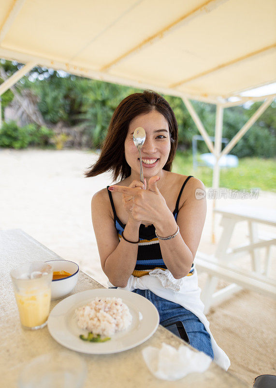 年轻女子在海滩上用咖喱勺模仿眼部检查