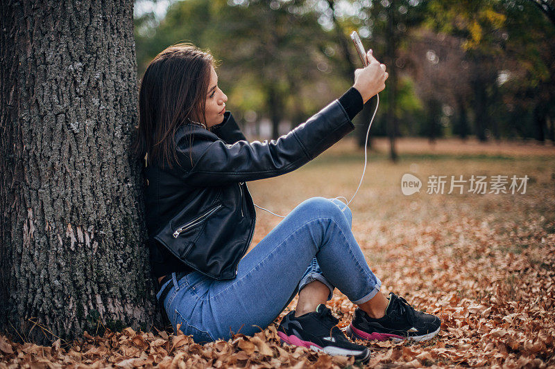 一个漂亮的年轻女子在公园里边自拍边听音乐。