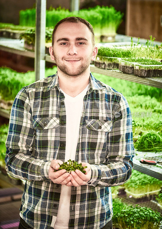 一个年轻人的肖像与葵花籽幼苗在他的手在温室