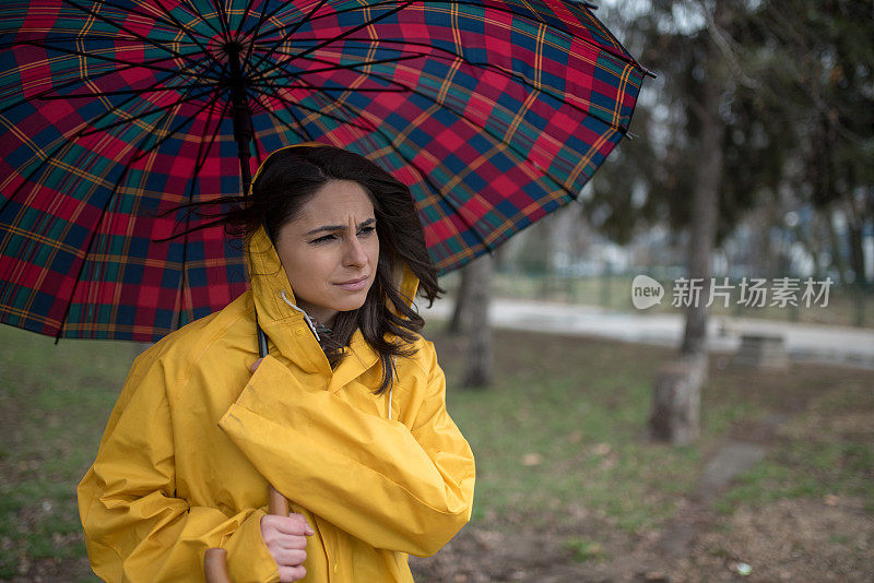 穿着黄色雨衣的年轻女子在公园里度过雨天