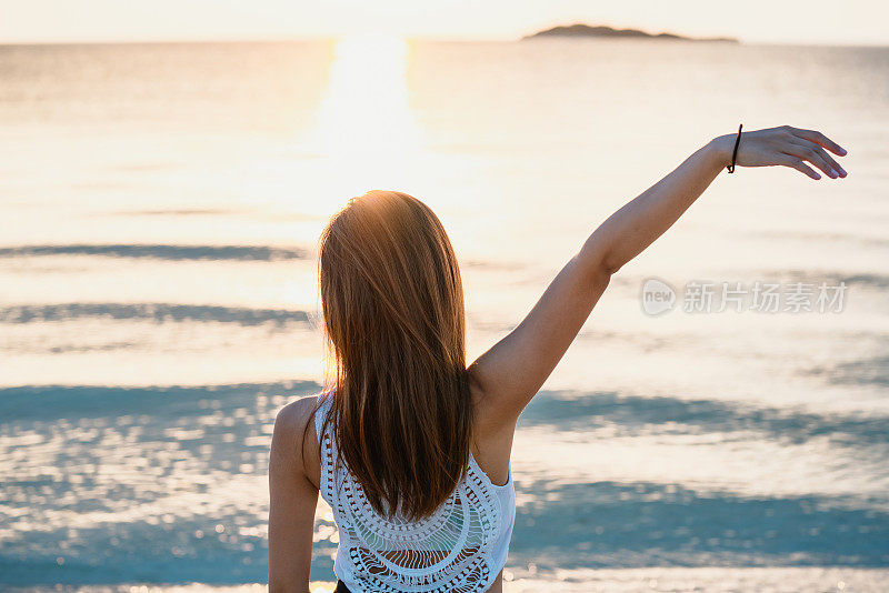 一个年轻女子的后视图，在日落时望向大海