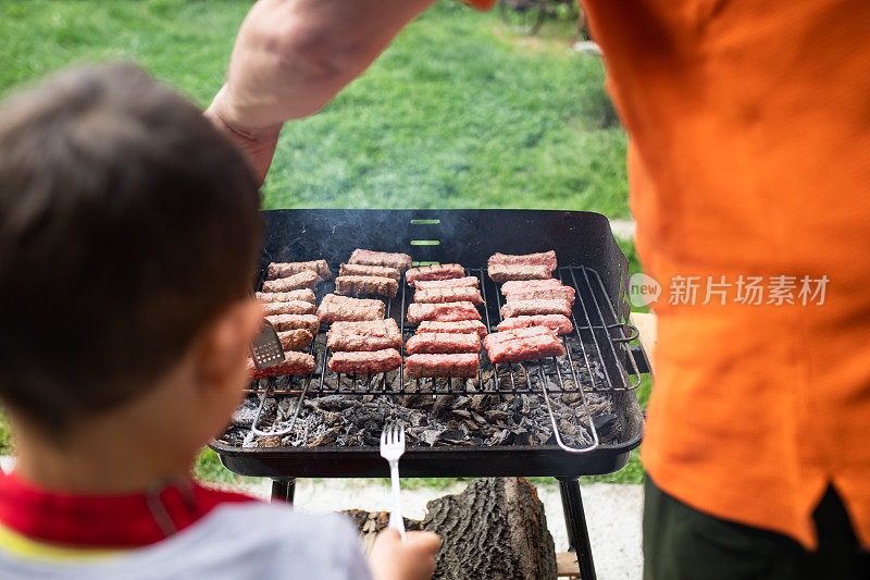 一个小男孩看着他的爷爷在烧烤上烤肉