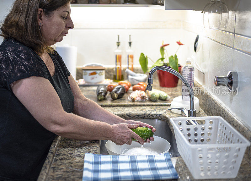 成年妇女在家庭厨房里洗蔬菜，然后把它们放进冰箱