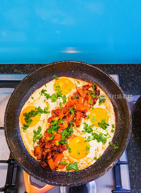 Shakshouka——用孜然调味的鸡蛋、番茄和香菜——在炉子上的煎锅里烹饪