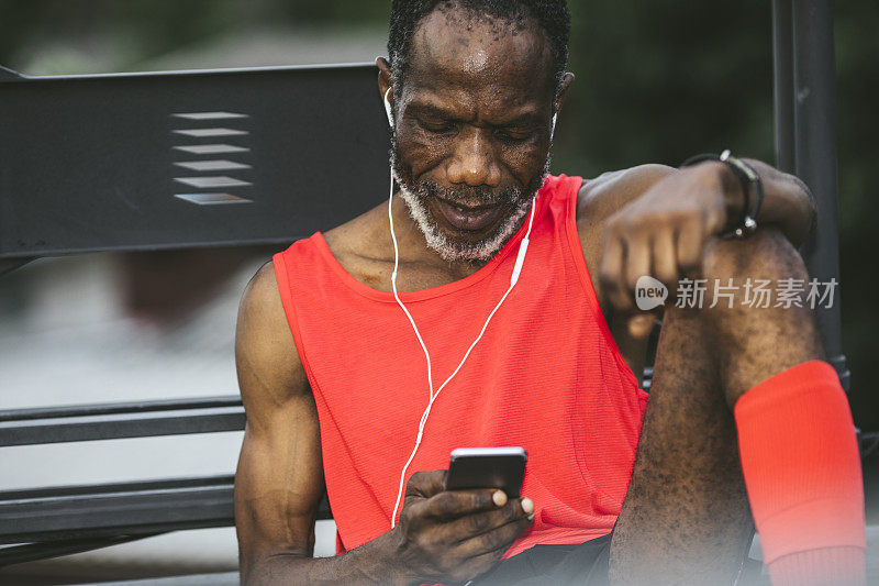 运动的老年男子在红色运动服在他的智能手机上发短信，同时听音乐后锻炼