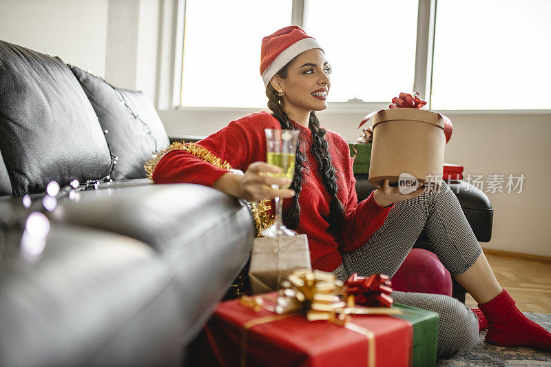 肖像的迷人微笑的女人喝香槟和打开她的圣诞或新年礼物