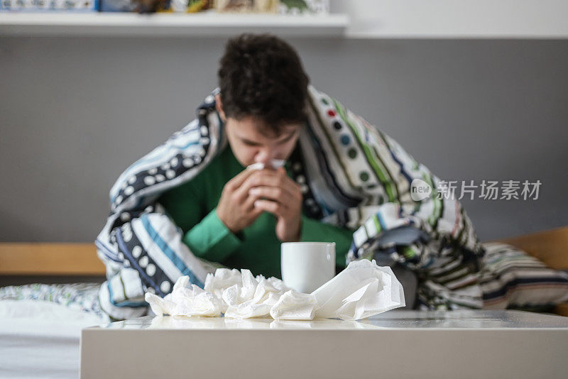 生病的小男孩坐在床上擤鼻涕