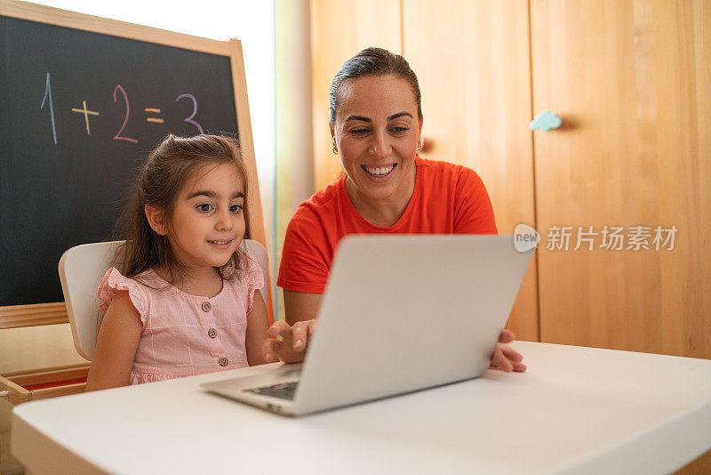 妈妈帮助和支持她的小女儿在家里用笔记本电脑上在线数学课