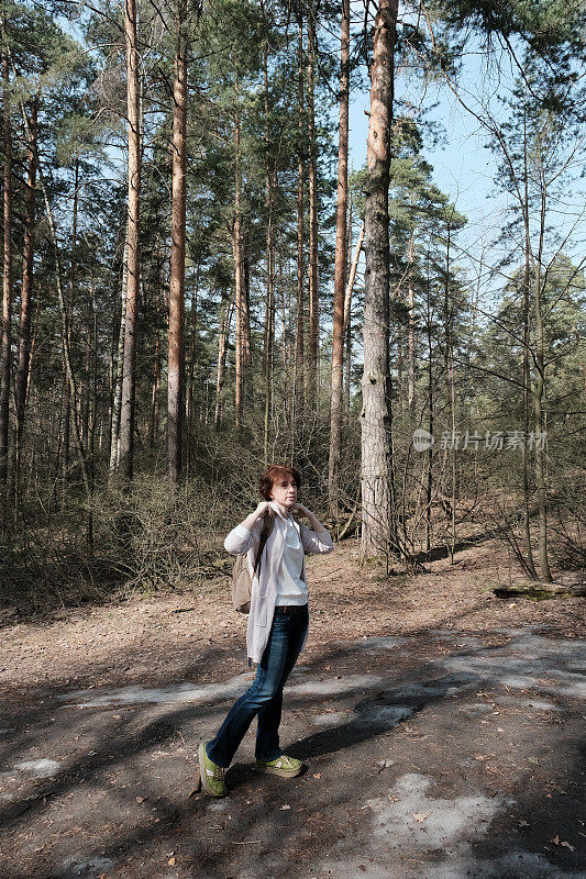 成熟的女人走在阳光明媚的森林里，站着环顾四周