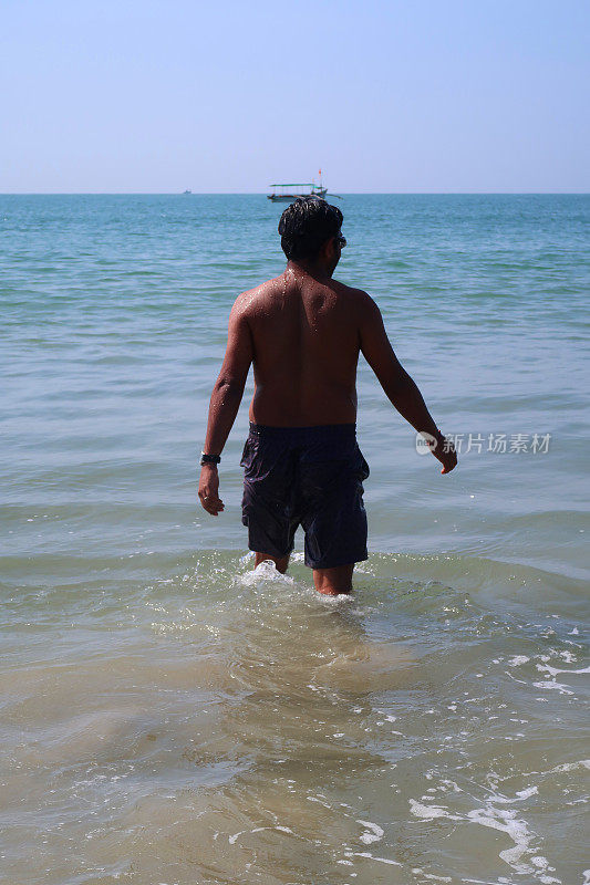 在印度果阿的Palolem海滩上，一名印度男子在海滩度假，当海浪卷到沙滩上时，他走到印度洋的海上