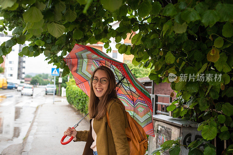 年轻女子享受散步，尽管雨在秋天的一天在城市