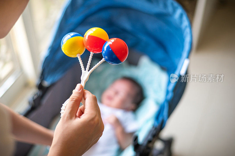 妈妈娱乐和平息愤怒的40天大男婴醒来，躺在窗户旁边的婴儿车