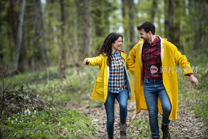 穿着雨衣的幸福情侣在大自然中牵着手旋转