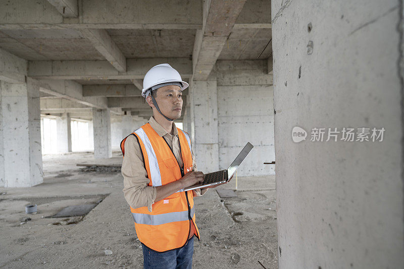 一位男性工程师在一座现代化办公楼的建筑工地用笔记本电脑工作。