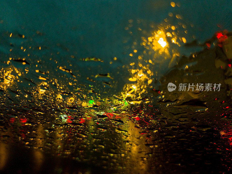 雨点落在汽车的挡风玻璃上。车水马龙，车灯倒映。