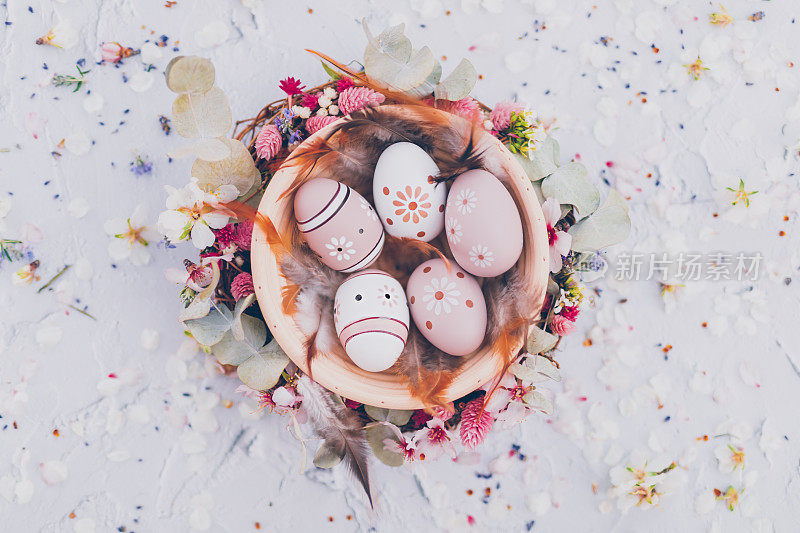 这是一个奇妙的扁平的碗，上面画着复活节彩蛋，用柔和的颜色和棕色的羽毛画着，周围是杏花和各种干花和树叶