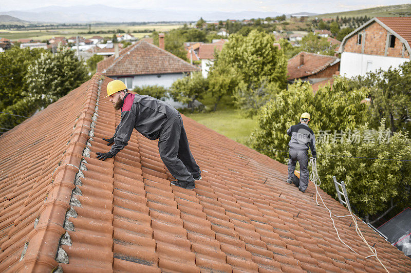 蓄胡子的工人在安装太阳能电池板前努力保持屋顶上的平衡