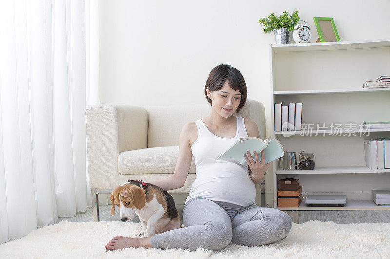 孕妇盘腿坐在地上边看书边抚摸宠物狗