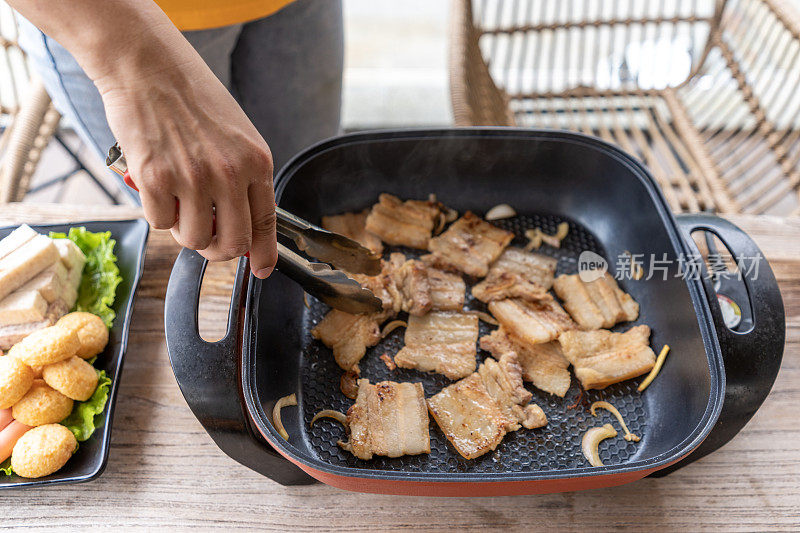 他一手拿着食物夹，在电饭锅里烤肉