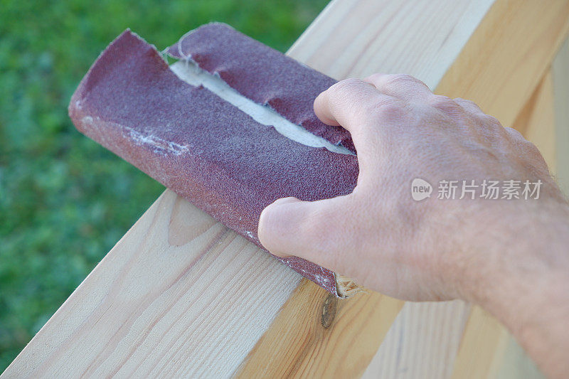 喷砂木头。一位男木匠正在打磨一座人造凉亭的木梁。近距离观察手的木匠摩擦木材与砂纸
