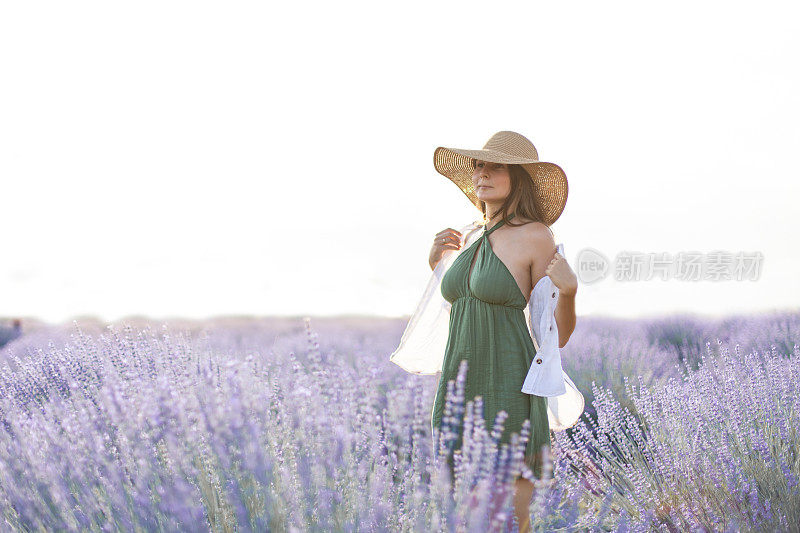 年轻女子穿着夏装，戴着太阳帽，透过薰衣草田的背影感到幸福