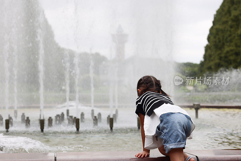 年轻的母亲和她的女儿在春天公园的喷泉旁玩耍