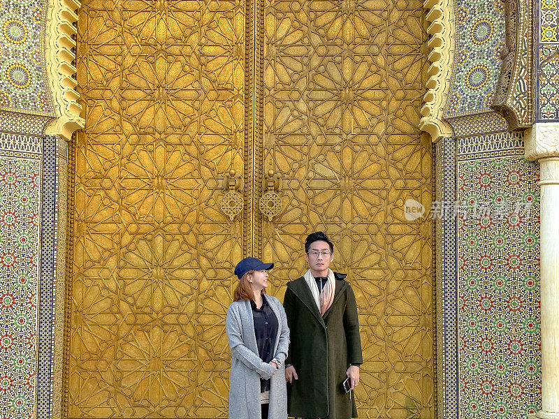 在摩洛哥菲斯，一对亚洲中国游客站在皇宫门口看镜头。